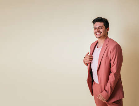 Handsome young man smiling dressed in a pink suit and T-shirt on a yellow background in a photo studio leaving a blank space to his rightの写真素材