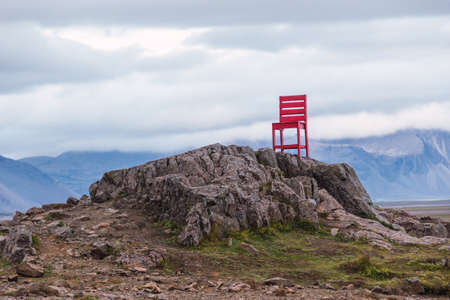 Sculpture of a red chair on the rocks located near townの写真素材