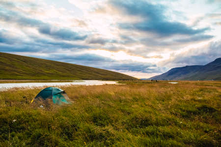 Green tent in a grassy meadow on the bank of a river in Iceland at sunsetの写真素材