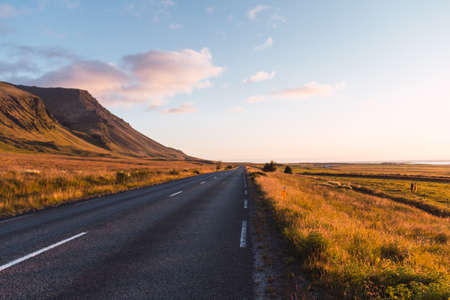 Asphalt road on a sunny day in Iceland with a hill in the backgroundの写真素材