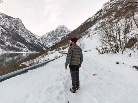 Young man standing in the snow by an icy lake in the snowy mountains of the Italian alps