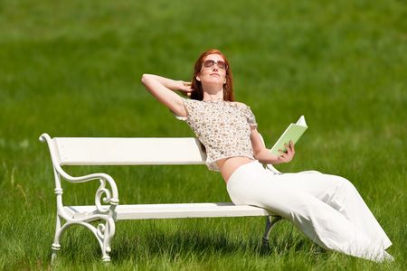 Red hair woman sitting with book on white bench in a meadow; shallow DOFの写真素材