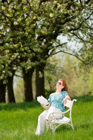 Red hair woman reading book on white bench in a meadow; shallow DOFの写真素材