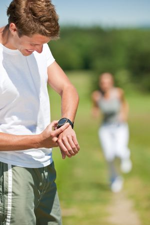 Young man with stopwatch measuring time, running woman in background, shallow DOFの写真素材