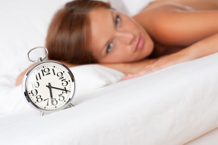 Alarm clock standing on bed, woman in background, shallow DOFの写真素材