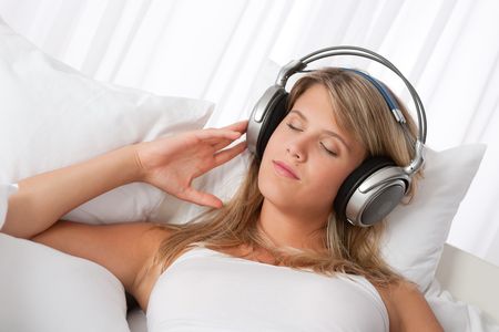 Blond woman with headphones listening to music lying on white sofaの写真素材