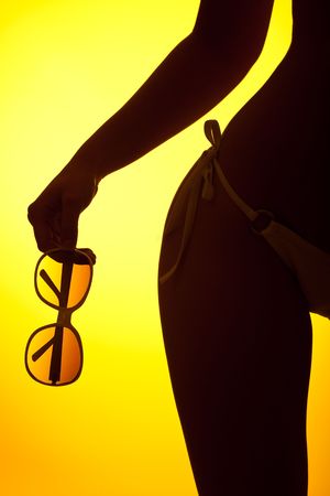 Silhouette of female body with bikini and sunglasses on yellow background, back litの写真素材