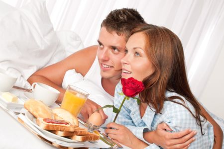 Happy man and woman having luxury hotel breakfast in bed togetherの写真素材
