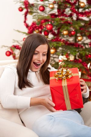 Surprised woman with Christmas gift in front of treeの写真素材