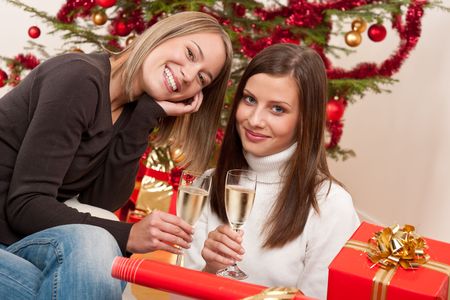 Two young woman with champagne and Christmas tree and presentの写真素材