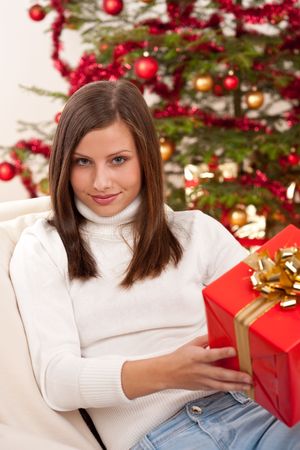 Young woman holding Christmas present in front of treeの写真素材