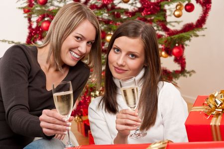 Two young woman with champagne and Christmas tree and presentの写真素材