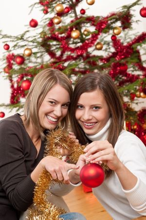 Two cheerful women with Christmas chains and balls in front of treeの写真素材
