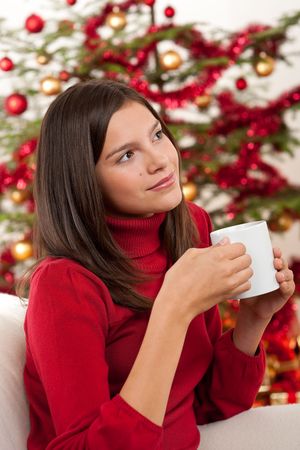 Attractive brunette in front of Christmas tree holding cup of coffeeの写真素材