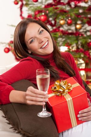 Smiling woman with Christmas present and glass of champagne in front of treeの写真素材