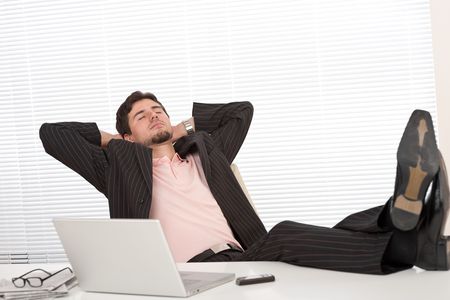 Young businessman in black suit relaxing at office with legs upの写真素材