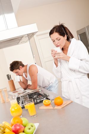 Woman having coffee for breakfast in the kitchen, man reading newspaper in backgroundの写真素材