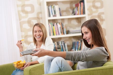 Students - Two female teenager watching television and eating crisps in modern loungeの写真素材