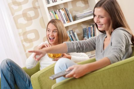 Students - Two smiling female teenager watching television in modern living roomの写真素材