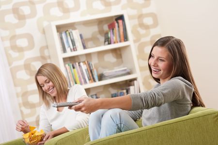 Students - Two smiling female teenager watching television in modern living roomの写真素材