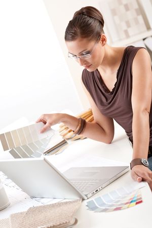 Smiling female designer with color swatch and laptop at officeの写真素材