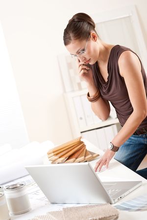 Female interior designer with laptop and phone working at officeの写真素材