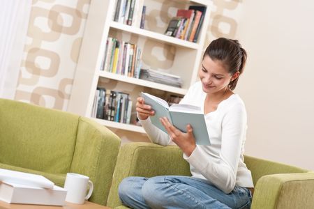 Students - Happy teenager with book sitting on armchair in loungeの写真素材