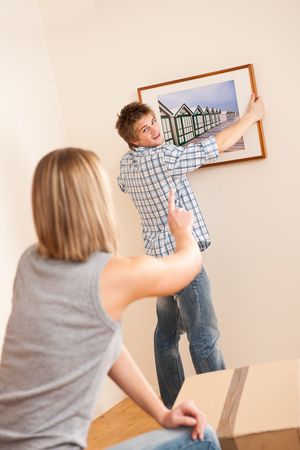 Moving house: Couple hanging picture on wall in new homeの写真素材
