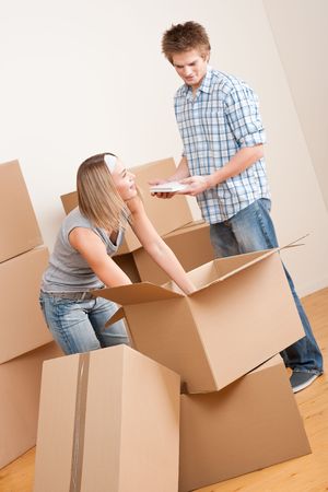 New house: Young couple with box in new home unpacking bookの写真素材