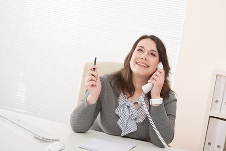 Smiling young business woman working on the phone at officeの写真素材