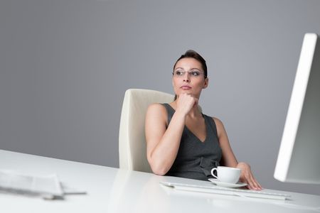 Successful business woman at office having cup of coffee sitting at computer deskの写真素材