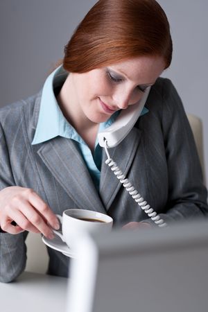 Successful businesswoman calling on the phone at office, having coffeeの写真素材