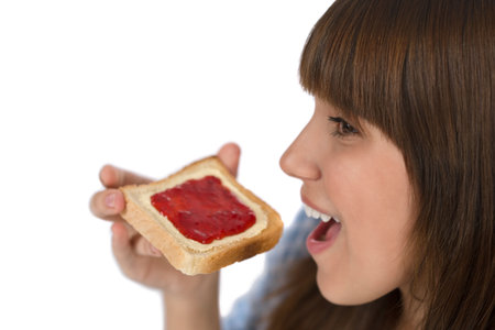 Happy teenager in pajamas eating healthy toast for breakfast on white background