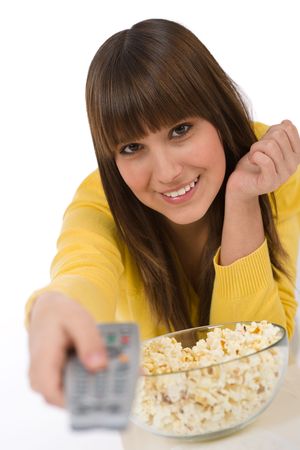Happy female teenager watching television holding remote control, eating popcornの写真素材