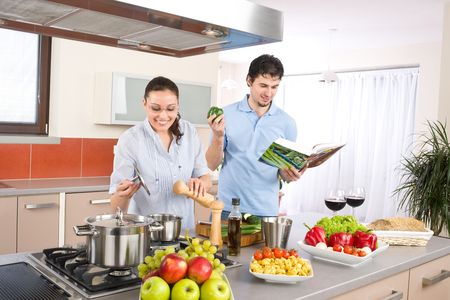 Young happy couple cook in kitchen with cookbook, pasta, vegetableの写真素材
