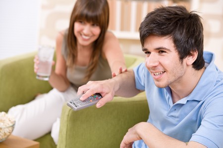 Student - happy teenagers watching television holding remote control in living roomの写真素材