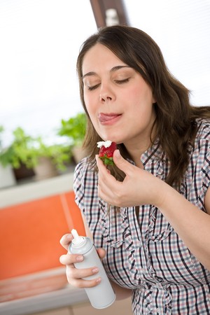 Plus size woman with whipped cream on strawberry licking lips in kitchenの写真素材