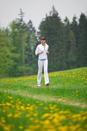 Jogging - sportive woman running in park with dandelion, listen to music with earbudsの写真素材