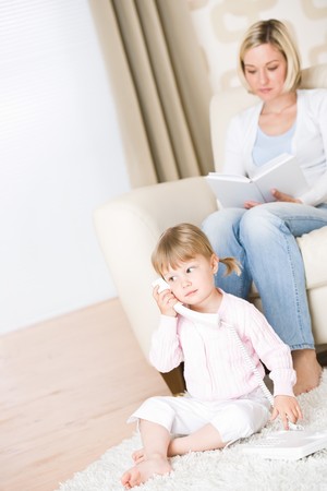 Mother and child - on the phone in living room with bookの写真素材