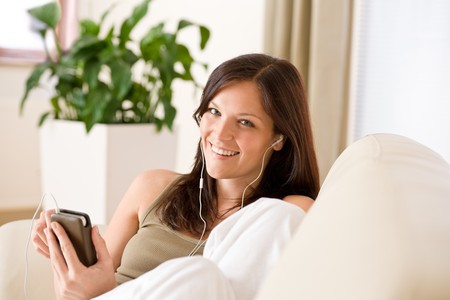 Woman holding music player listening with earbuds lying down on sofa homeの写真素材
