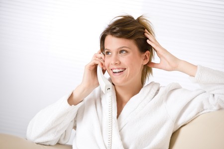 Happy woman in white bathrobe with phone home calling in loungeの写真素材