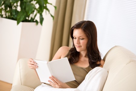 Young happy woman read book on sofa in living roomの写真素材