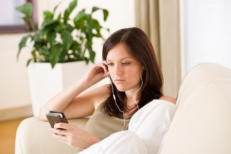 Woman holding music player listening with earbuds home, plant in backgroundの写真素材