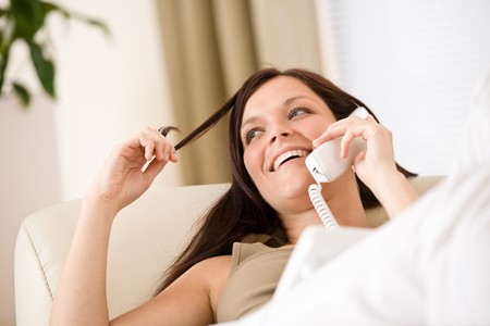 On the phone home: Smiling woman on sofa calling, plant in backgroundの写真素材