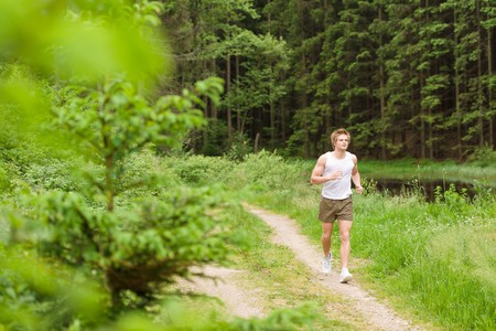 Sportive man jogging in nature by lake in sportive outfitの写真素材