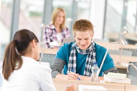 Three high school students in classroom studying with books and laptopの写真素材