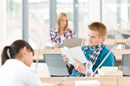 Three high school students in classroom studying with books and laptop
