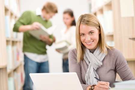 High school library - happy female student with laptop and bookの写真素材