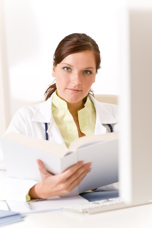 Female doctor read book in clinic sitting at deskの写真素材