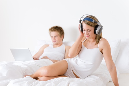 Young couple relax in bed with music and laptop togetherの写真素材